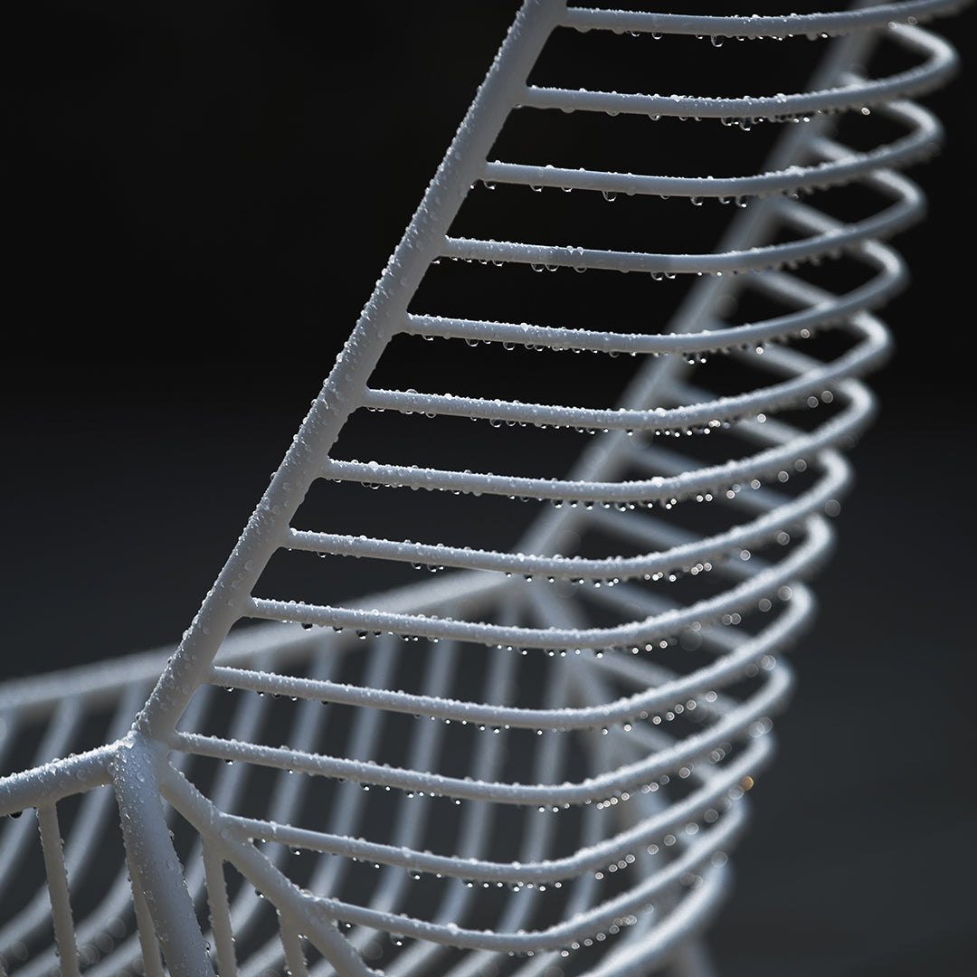 White wire basket with sleek spiral pattern and glistening droplets, set against a dark background.