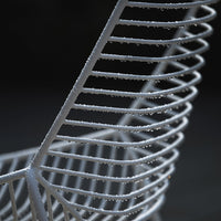 White wire basket with sleek spiral pattern and glistening droplets, set against a dark background.