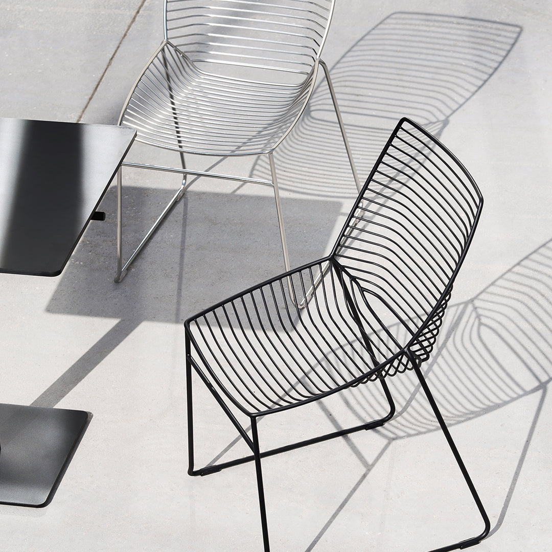 "Modern wire chairs in black and silver with sleek lines and minimalist design on a light gray surface."