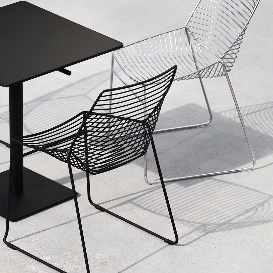 Modern black wire chair and sleek white wire chair beside a minimalist black table, showcasing elegant lines and shadows.