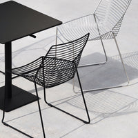 Modern black wire chair and sleek white wire chair beside a minimalist black table, showcasing elegant lines and shadows.