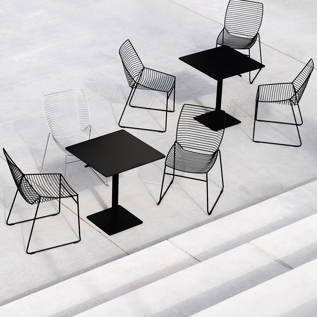 Black metal table with wire mesh chairs, featuring sleek lines and geometric patterns against a neutral concrete background.