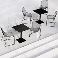 Black metal table with wire mesh chairs, featuring sleek lines and geometric patterns against a neutral concrete background.