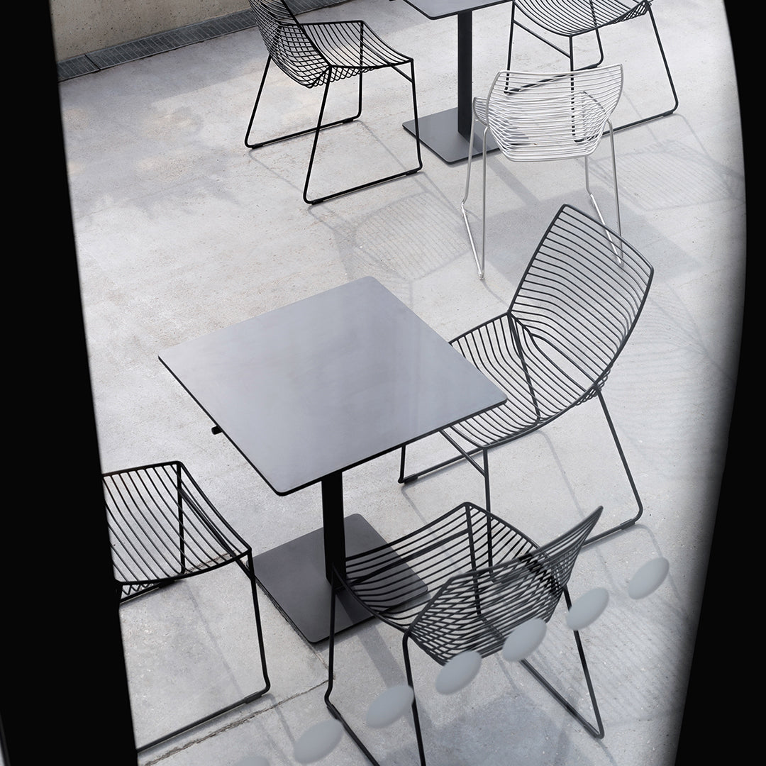 Modern black metal table and wire chairs with sleek lines and minimalistic design, set on a concrete floor.