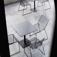 Modern black metal table and wire chairs with sleek lines and minimalistic design, set on a concrete floor.