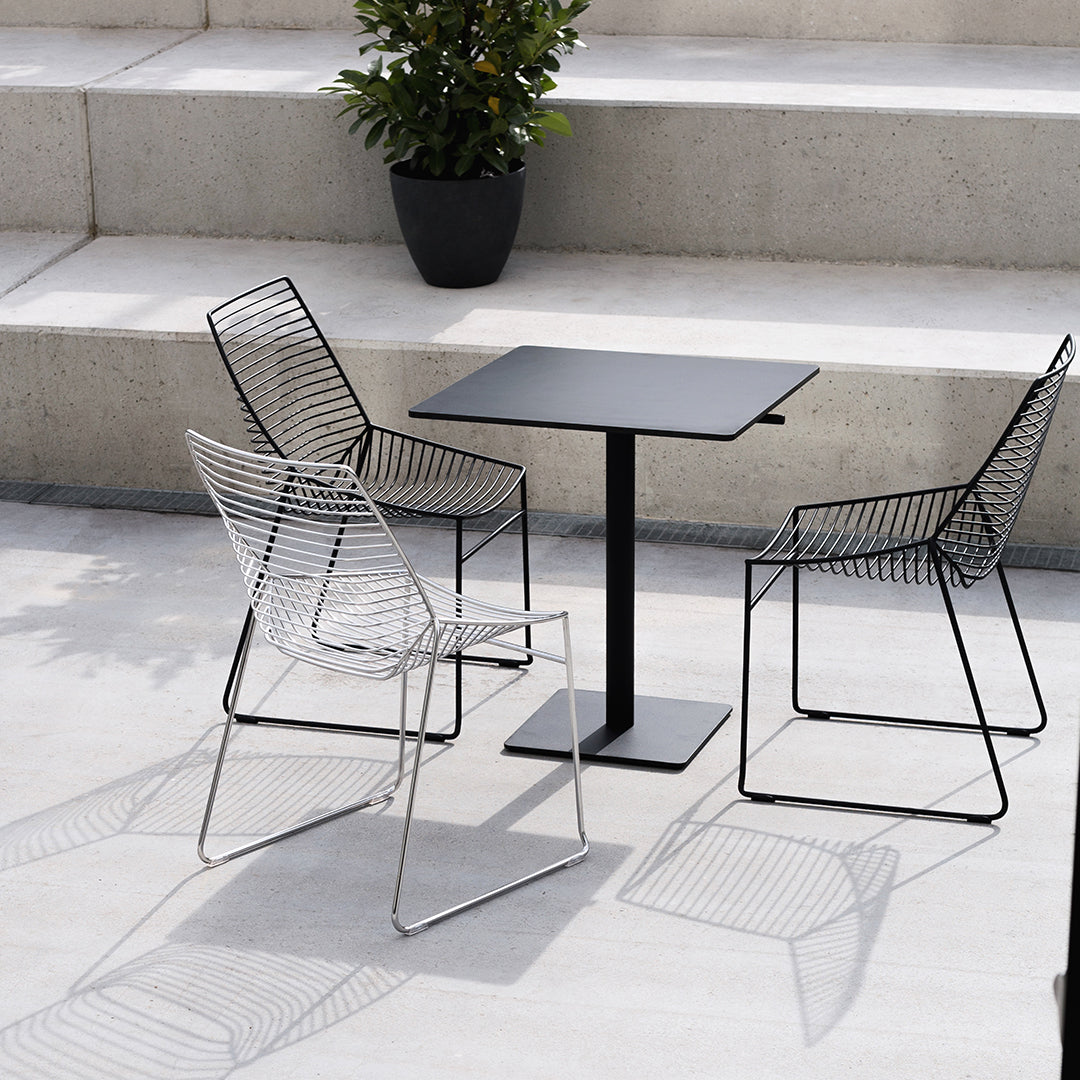 "Modern black table with minimalistic wire chairs in sleek black and white patterns, set against a neutral stone background."