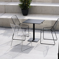 "Modern black table with minimalistic wire chairs in sleek black and white patterns, set against a neutral stone background."