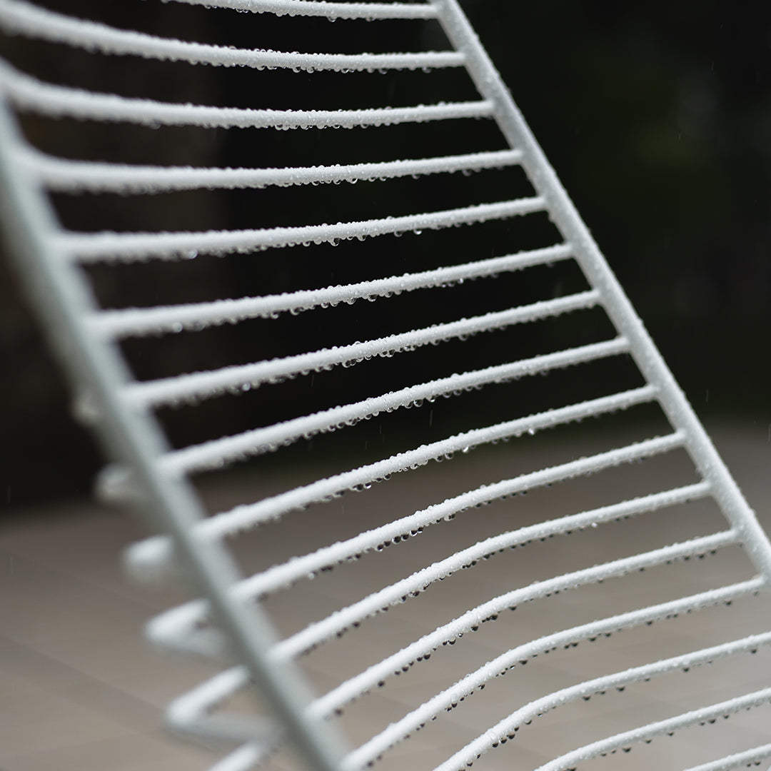 "White striped metal chair, featuring a sleek pattern with evenly spaced lines, set against a blurred dark background."