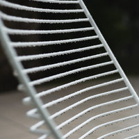 "White striped metal chair, featuring a sleek pattern with evenly spaced lines, set against a blurred dark background."