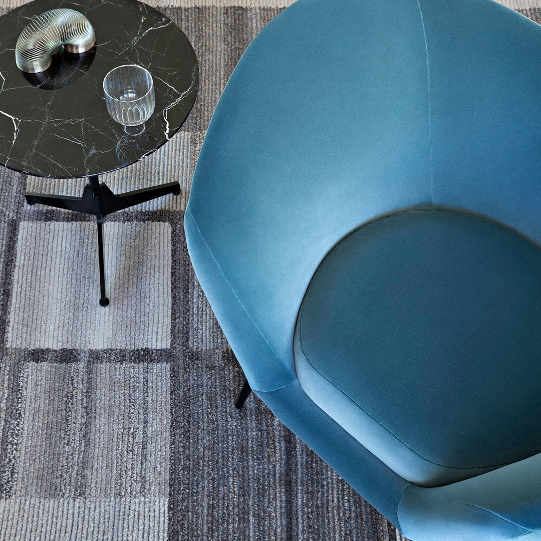 Aqua blue chair with a smooth finish, paired with a geometric grey patterned rug and a sleek black side table.