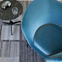 Aqua blue chair with a smooth finish, paired with a geometric grey patterned rug and a sleek black side table.