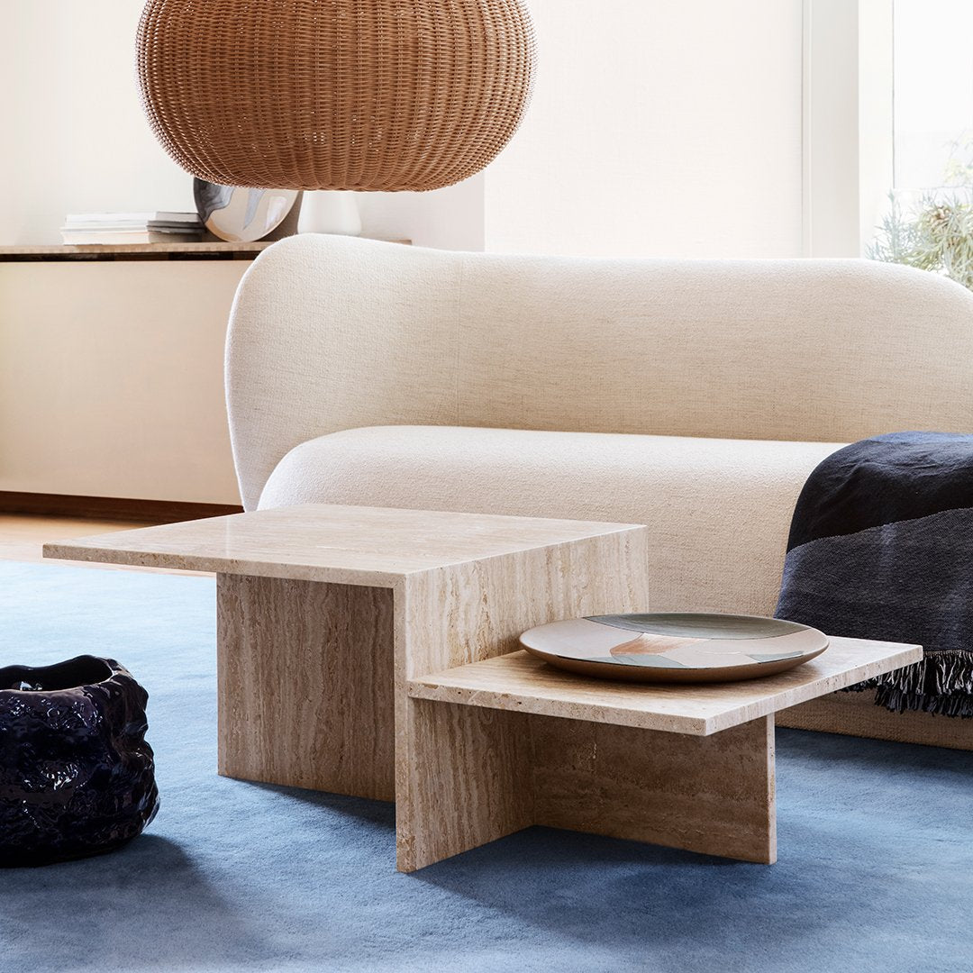 Natural wood coffee table with a light beige finish, featuring clean lines and a minimalist design. Soft blue rug backdrop.