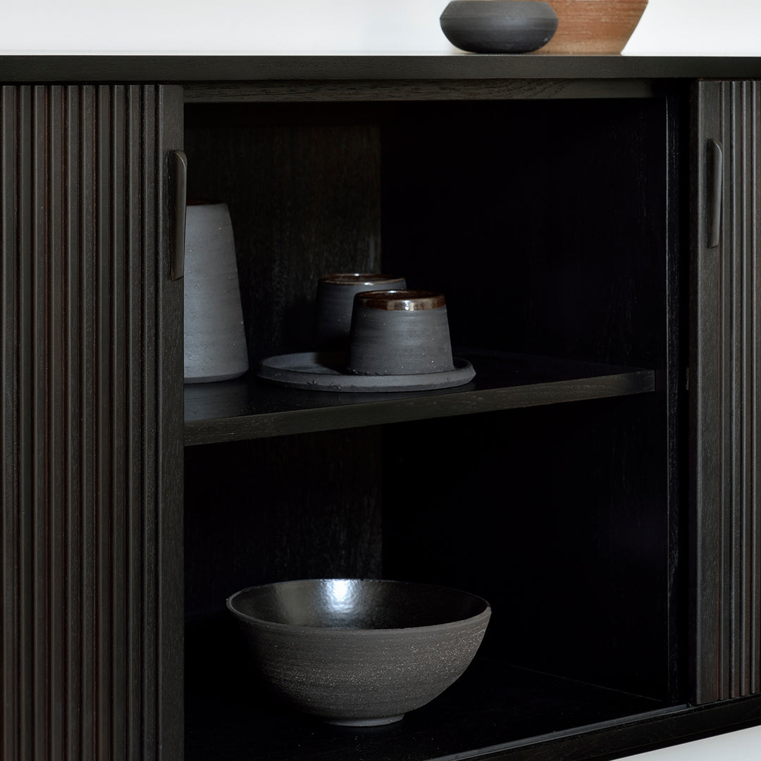 "Modern black cabinet with ribbed texture, featuring gray ceramic bowls and vases in subtle earth tones."