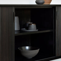 "Modern black cabinet with ribbed texture, featuring gray ceramic bowls and vases in subtle earth tones."
