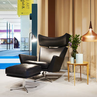 Black leather chair with sleek lines, complemented by a light-colored wooden side table and soft beige curtains.