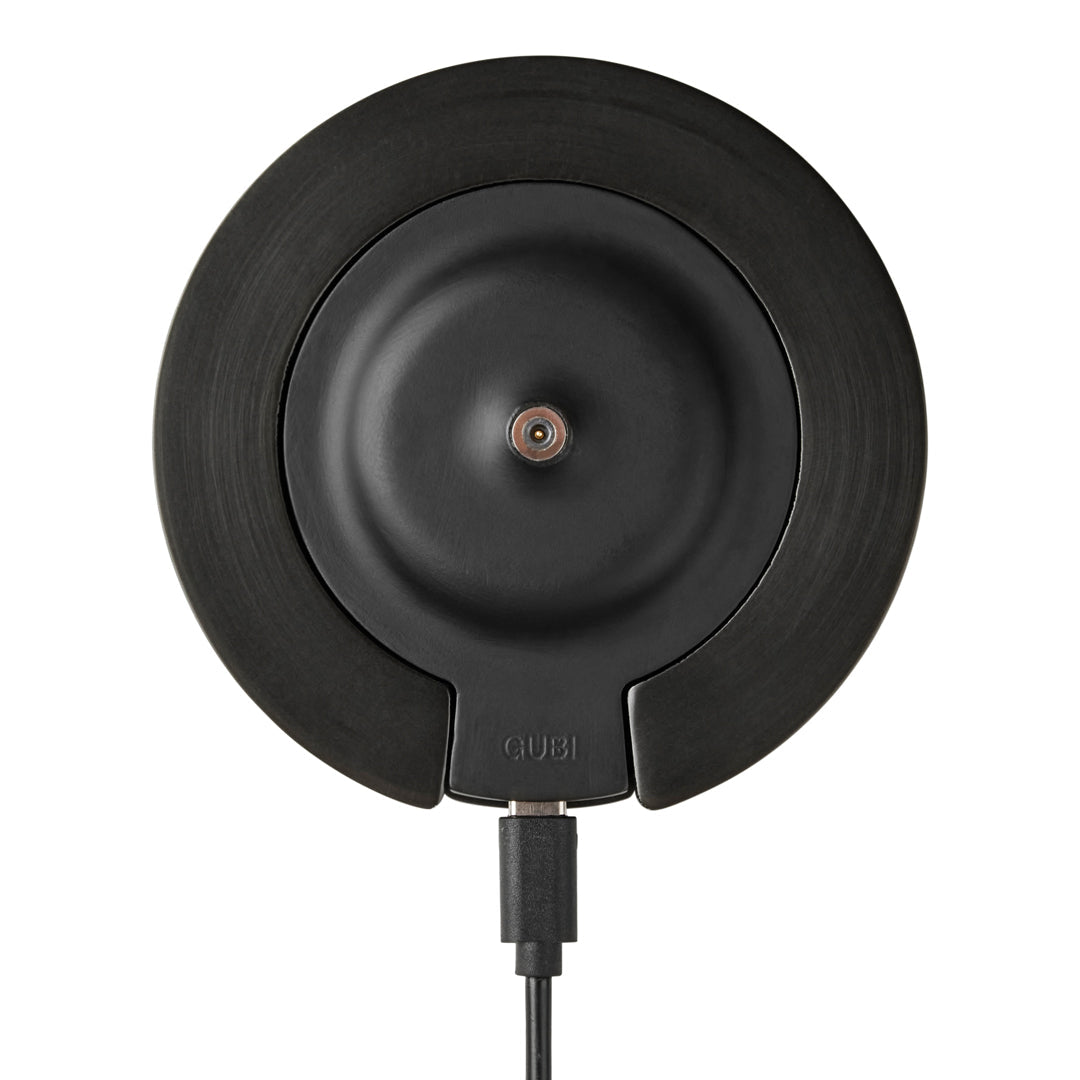 Black circular charging pad with a smooth matte finish and subtle textures, featuring a centered copper accent.