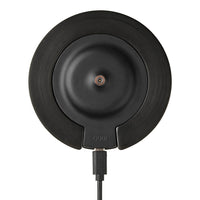 Black circular charging pad with a smooth matte finish and subtle textures, featuring a centered copper accent.