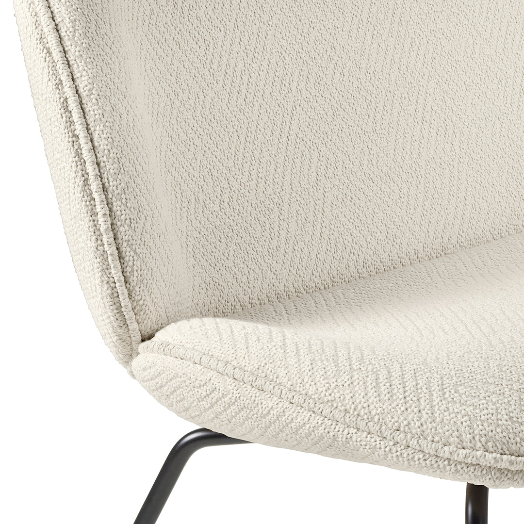 Textured cream upholstery with a herringbone pattern on a modern chair. Black metal legs complement the design.