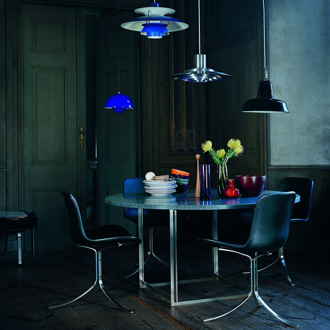 Modern dining room with a round blue table, black chairs, and colorful pendant lights in a soft, neutral space.