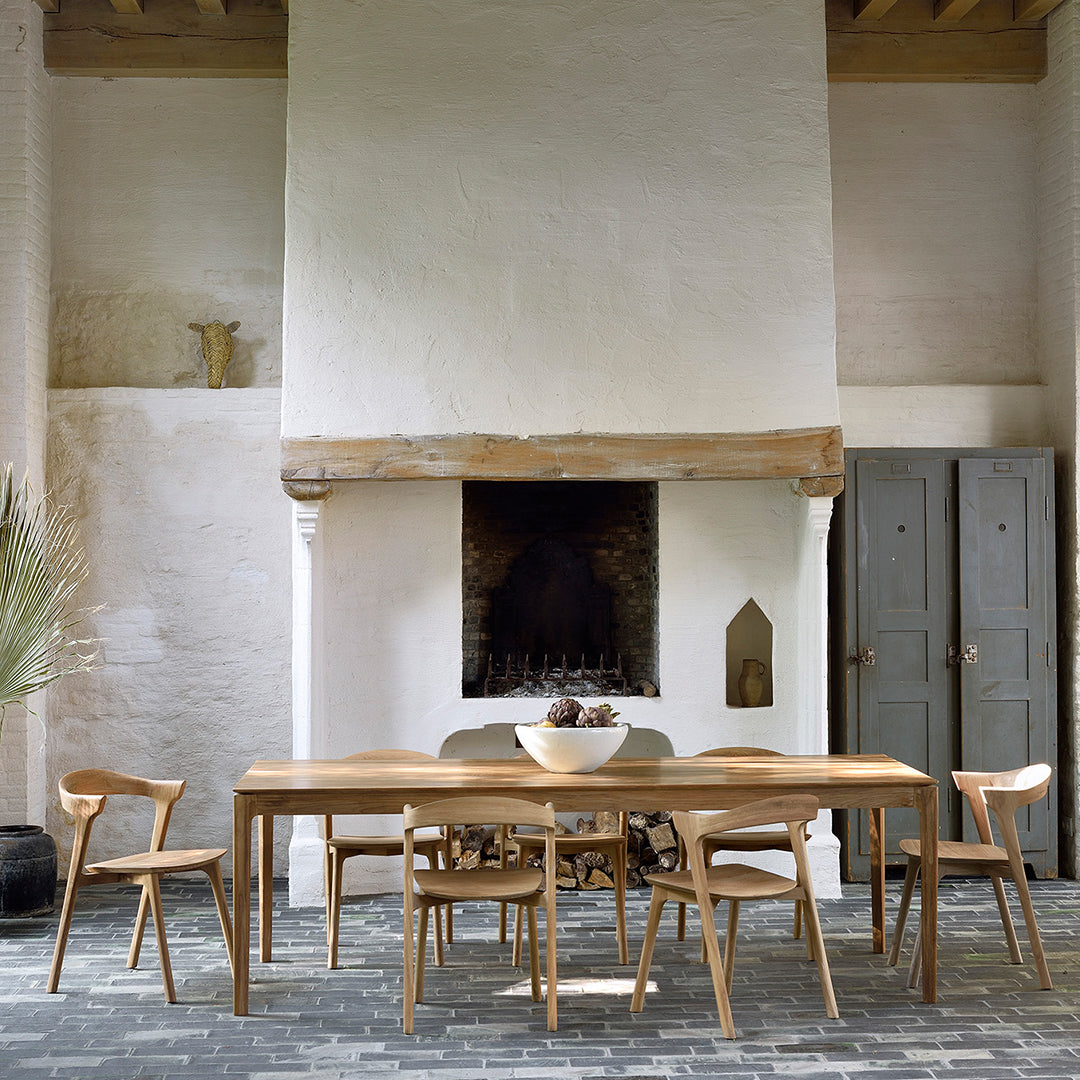 Elegant wooden dining table with light brown tones, featuring simple lines in a neutral, textured room setting.