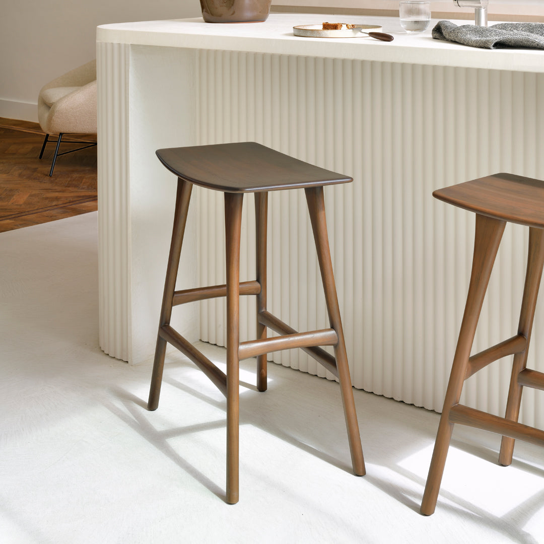 Brown wooden bar stools with sleek, minimal design against a light-colored backdrop featuring textured patterns.