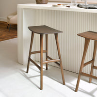 Brown wooden bar stools with sleek, minimal design against a light-colored backdrop featuring textured patterns.