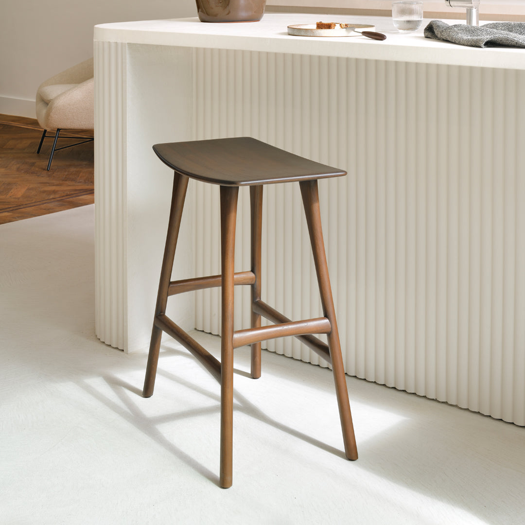 Dark brown wooden bar stool with smooth, curved seat and tapered legs, complementing a minimalistic white backdrop.