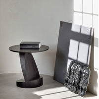 Stylish black round side table with smooth curves, paired with a textured monochrome art piece and soft blanket.