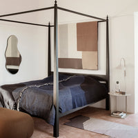 "Modern bed with a dark blue, gray, and taupe patterned duvet against neutral walls and soft beige flooring."