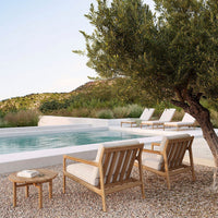 "Neutral-toned lounge chairs with cream cushions beside a serene blue pool and green olive trees, set in a natural landscape."