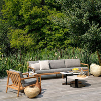 "Neutral gray sofa with light cushions, natural wood accents, and a round black and white table, set in a green outdoor landscape."