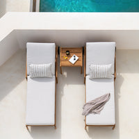 Sunlight grey lounge chairs with striped accent pillows, paired with a wooden side table by a turquoise pool.