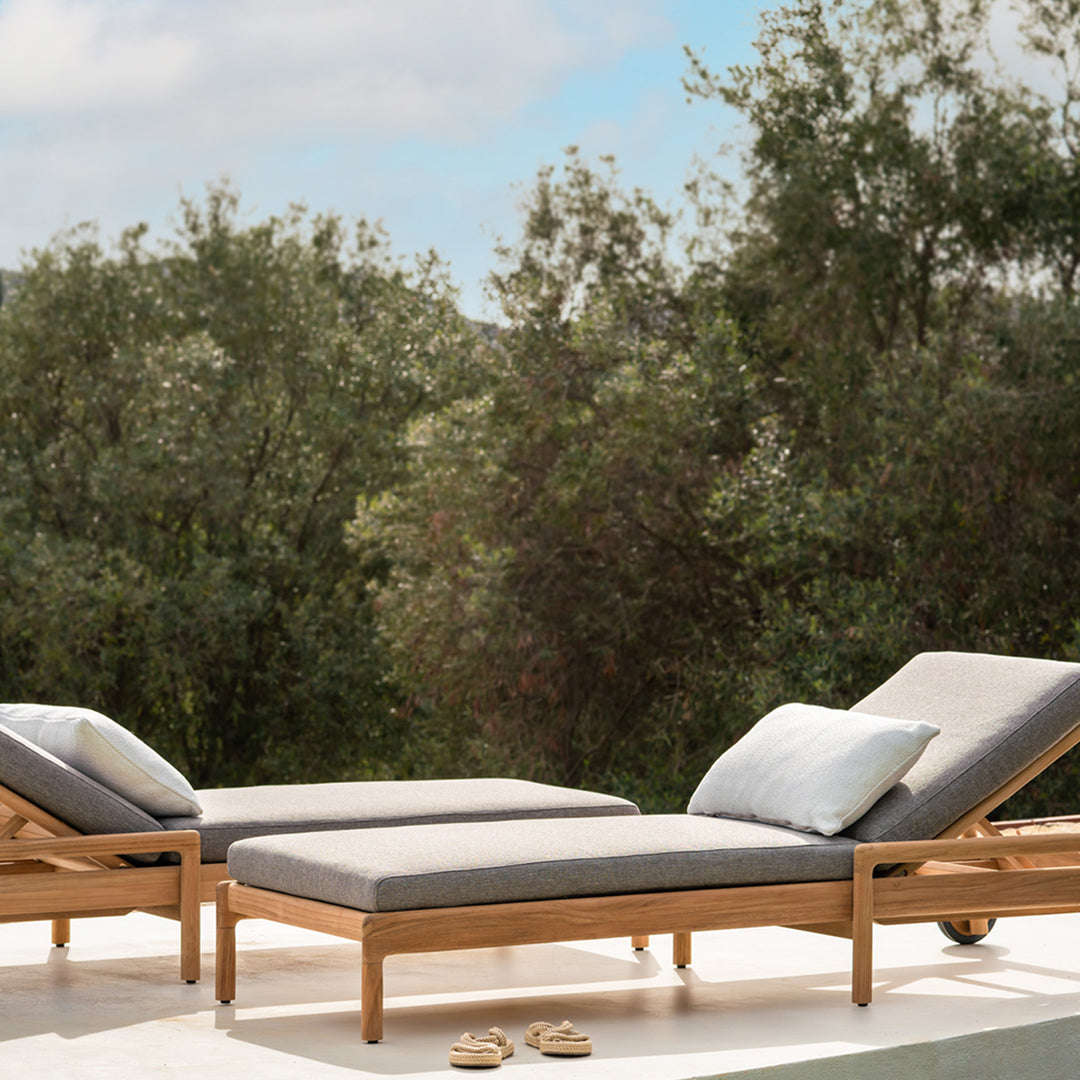 Light grey cushions on natural wood loungers against a serene green backdrop, perfect for outdoor relaxation.