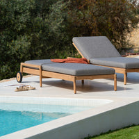 Gray outdoor chaise lounge with a textured fabric, paired with a warm orange throw, set against a serene blue pool.