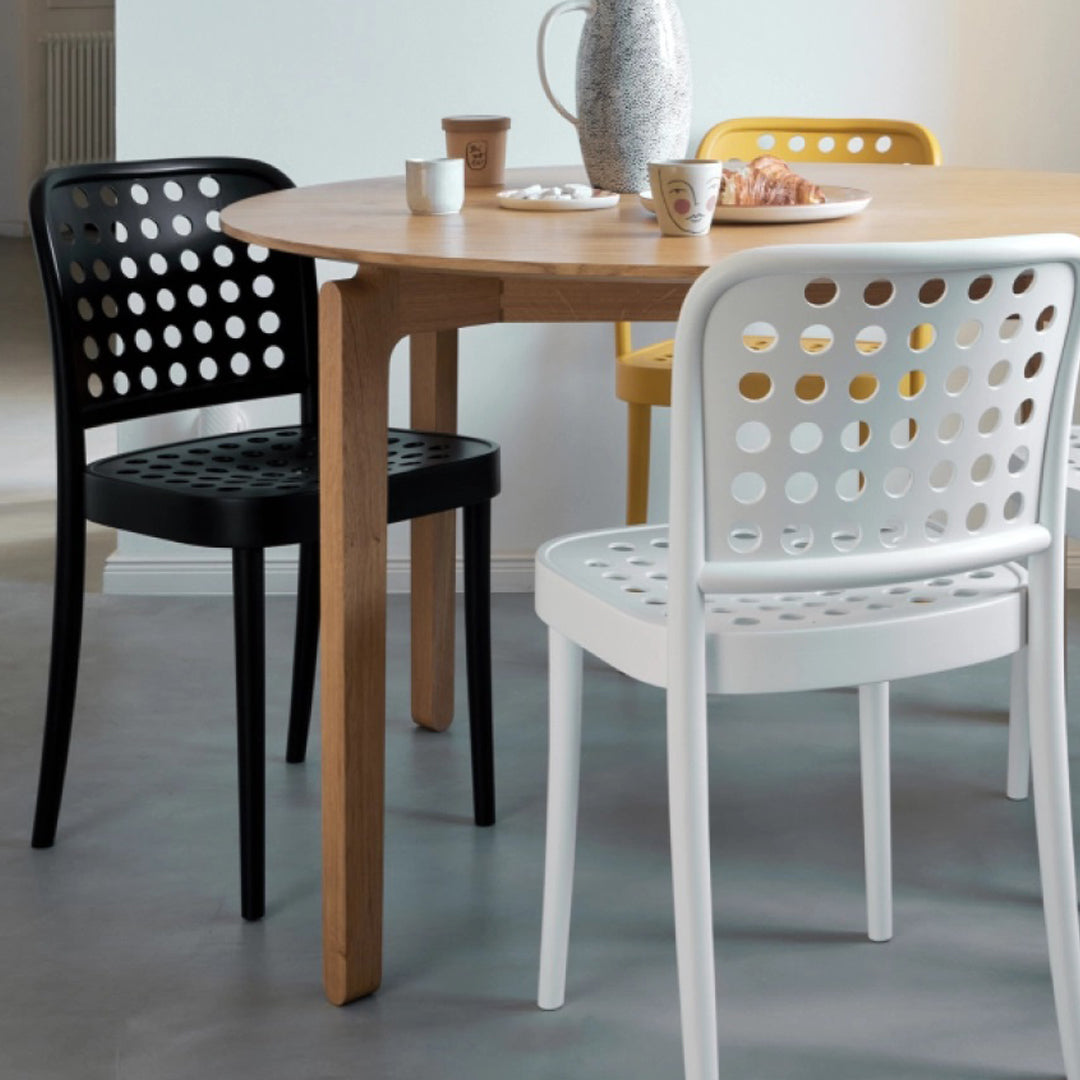 "Colorful perforated dining chairs in black, white, and yellow around a wooden table with circular patterns."