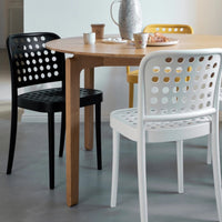 "Colorful perforated dining chairs in black, white, and yellow around a wooden table with circular patterns."
