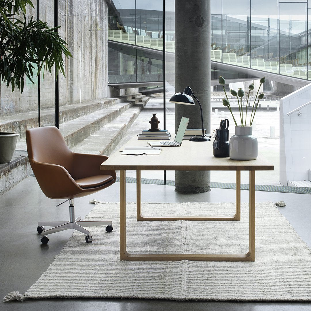 Modern office setting featuring a brown chair, white desk, and neutral rug in a minimalist, industrial backdrop.