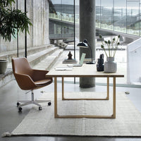 Modern office setting featuring a brown chair, white desk, and neutral rug in a minimalist, industrial backdrop.