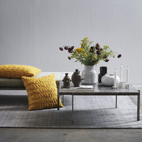 Yellow textured cushions on a neutral couch, with a vibrant flower arrangement and minimalist decor in soft tones.