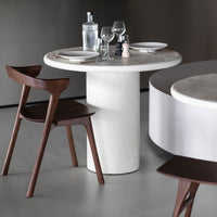 Round concrete dining table with sleek white surface, paired with dark wood chairs, set on a neutral gray floor.