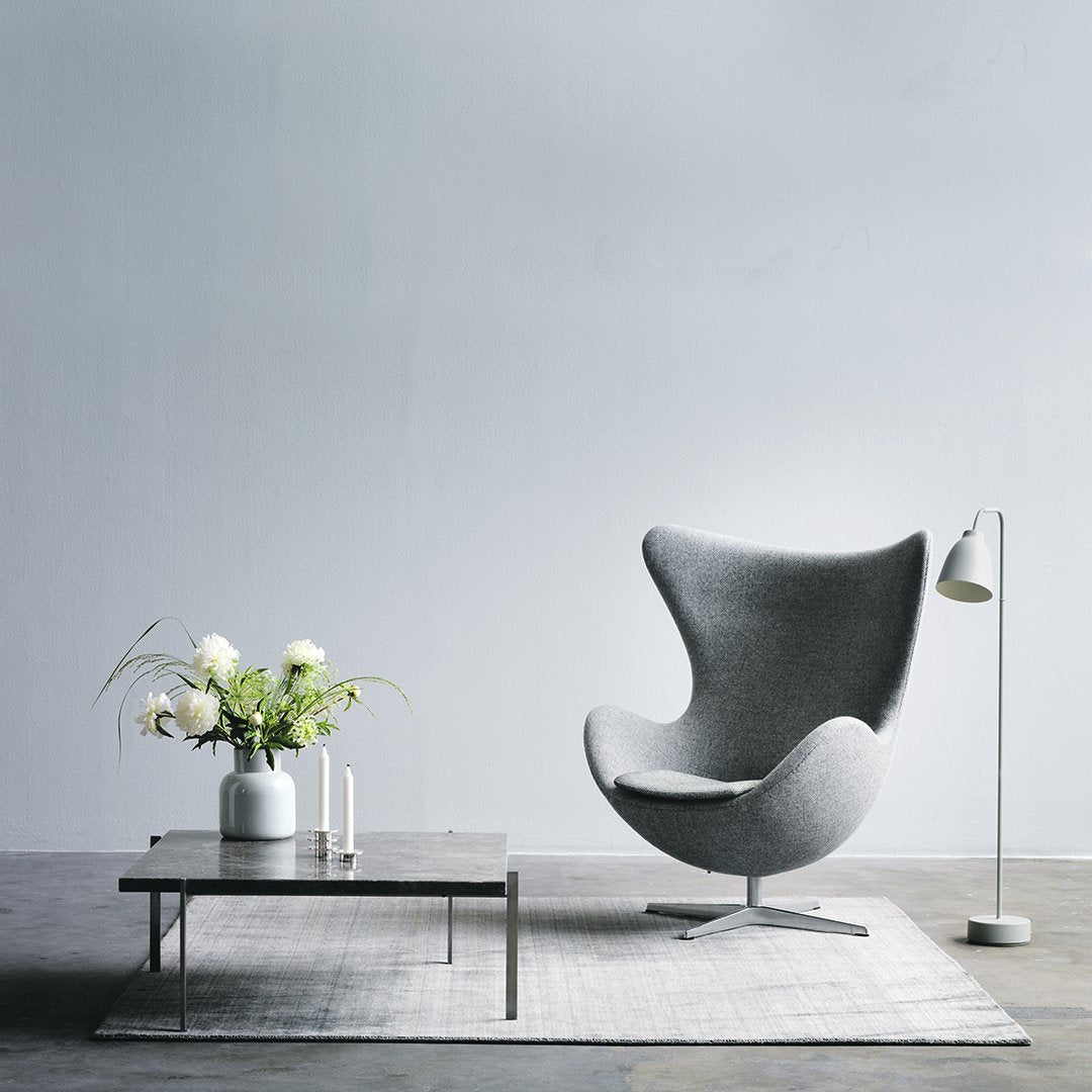 Gray accent chair with a smooth, modern design, set against a minimalist backdrop and paired with a white table and plant.