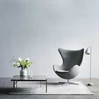 Gray accent chair with a smooth, modern design, set against a minimalist backdrop and paired with a white table and plant.