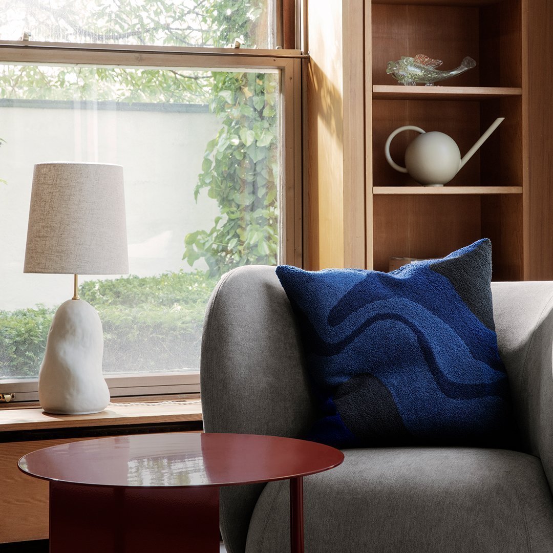 Sleek blue and gray patterned cushion on a modern gray sofa, accented by a minimalistic lamp and red table.