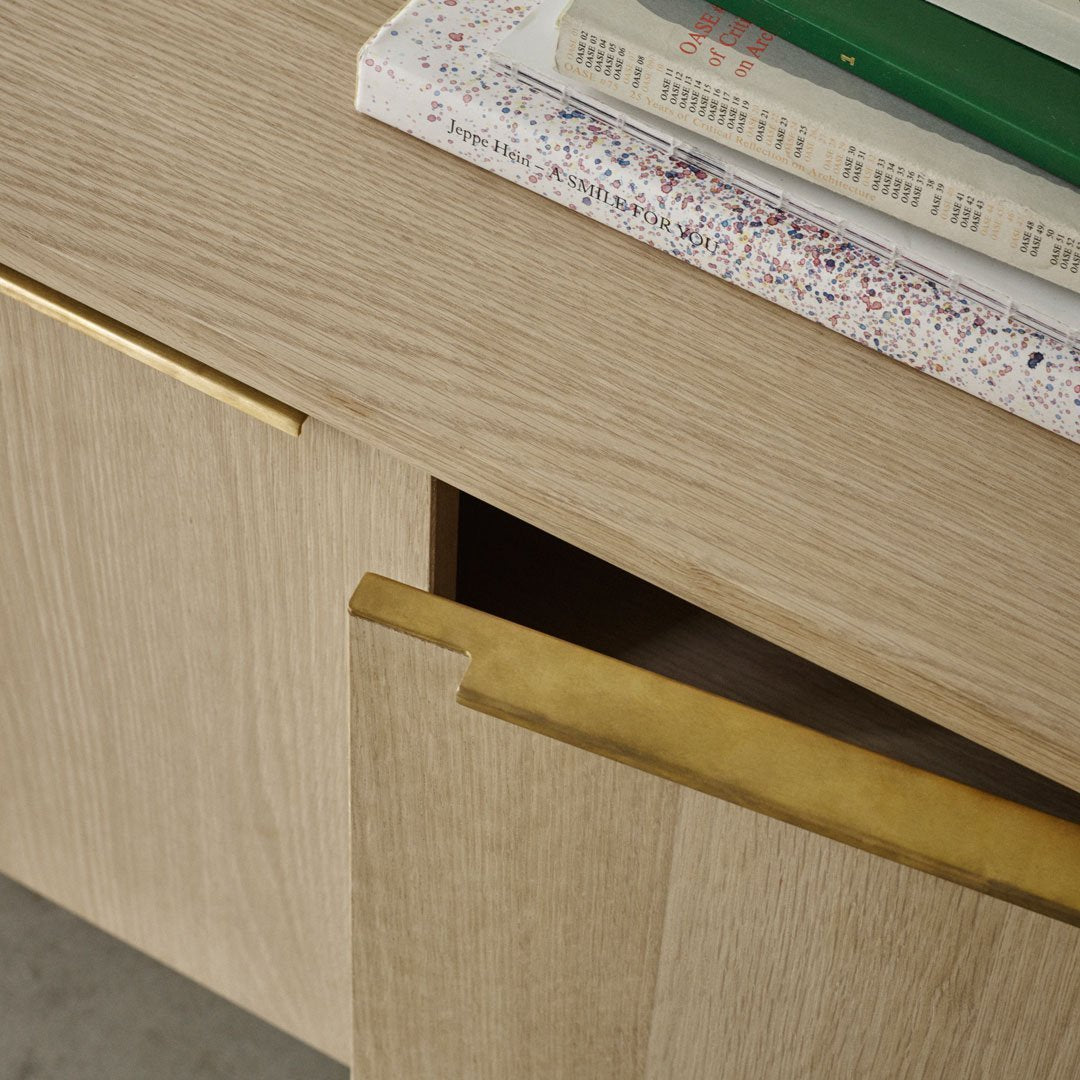 Natural wood grain with soft beige tones and brass handles, topped with colorful patterned books.