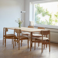 Light wood dining table with matching chairs in a minimalist setting, accented by greenery and natural light.