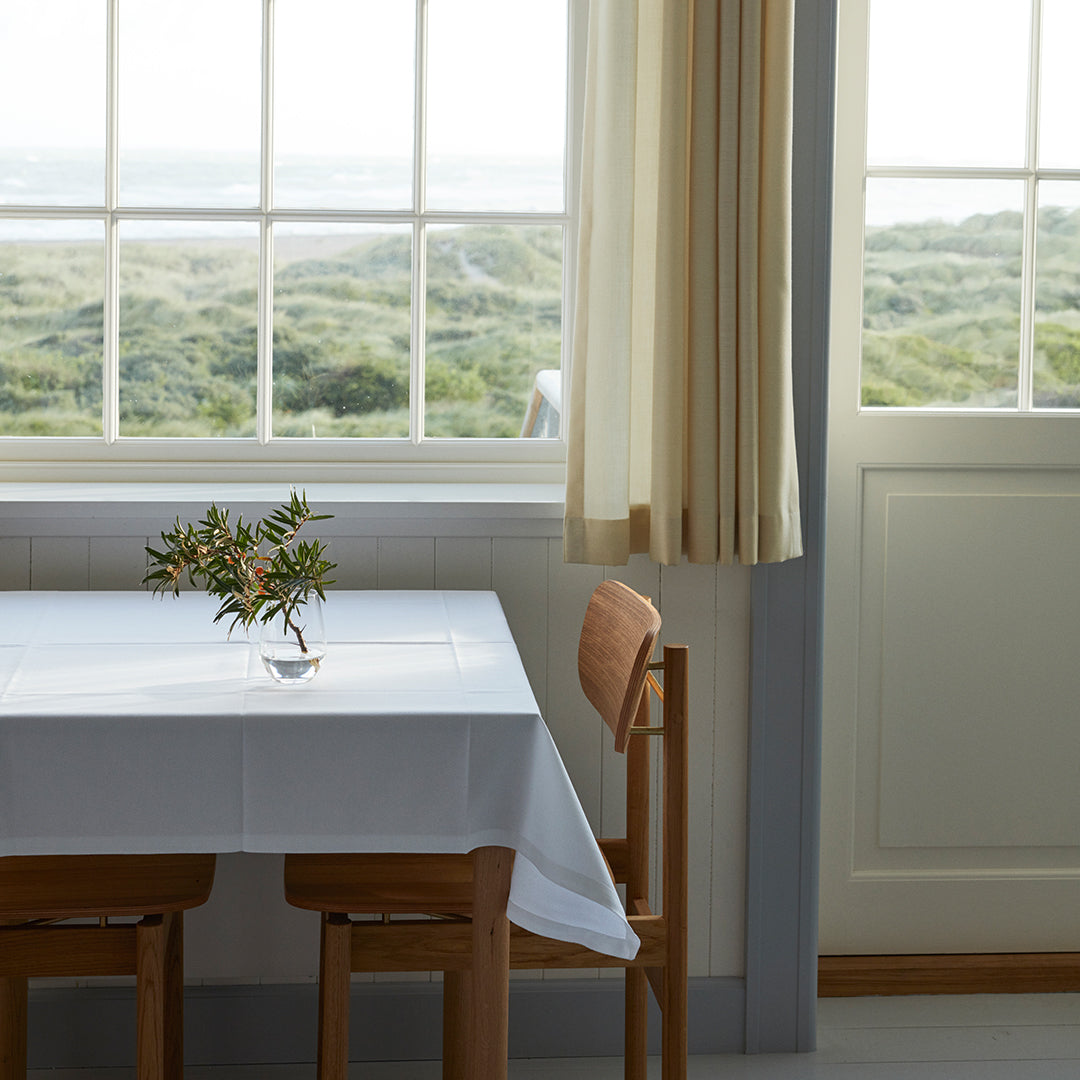 Elegant white table linen with crisp, clean lines, set against a serene backdrop of muted greens and natural wood tones.