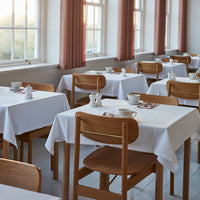 White tablecloths with light wood chairs, complemented by soft, muted pink curtains in a bright, airy dining space.