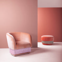 Peach velvet chair and ottoman with pink and lavender fringes against warm terracotta backgrounds. Soft, modern design.