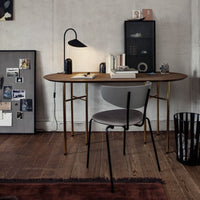 Modern desk with a smooth wood surface, gray chair, black lamp, and dark brown rug, set against neutral walls.