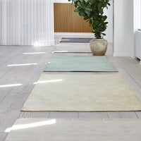 Assorted area rugs in soft green, cream, and gray tones, arranged on a light wood floor with natural light.